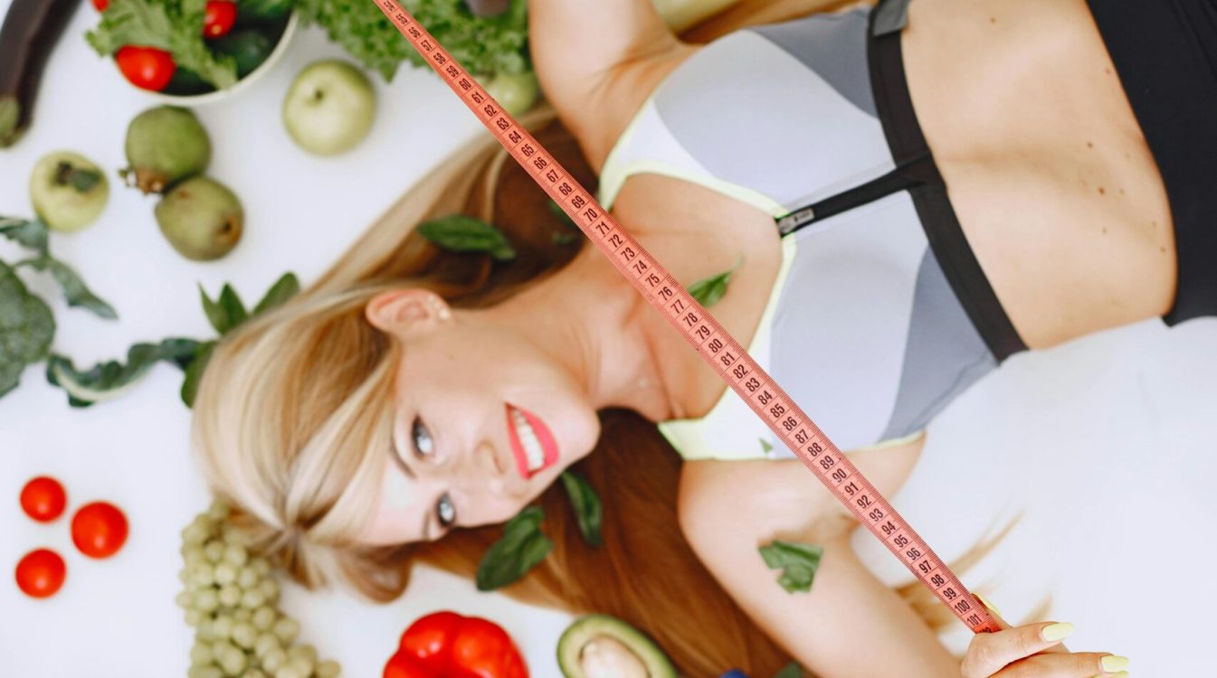 Woman lying with fruits and vegetables holding a measuring tape symbolizing a healthy lifestyle.
